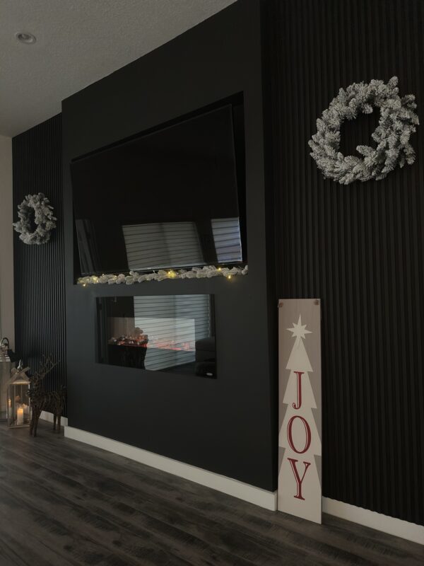 A black wall with a fireplace and christmas wreath.